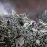 Emergency responders in protective gear clearing debris from a destroyed building in Ukraine following a drone attack.