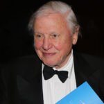 A realistic photograph of Sir David Attenborough standing outdoors alongside wildlife photographer Bence Máté, both looking at a camera display.